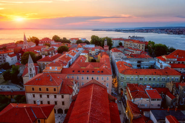 Top view of Zadar old town at sunset from the tower of Zadar cathedral, Dalmatia, Croatia. Scenic cityscape with historical architecture, red tiled roofs, sea, sky and sun, outdoor travel background